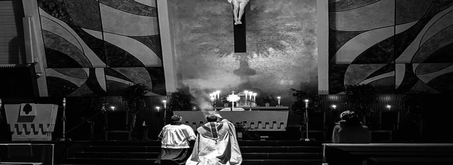 Benediction: two ministers kneeling before the Blessed Sacrament exposed in a monstrance on the altar, beneath a crucifix.